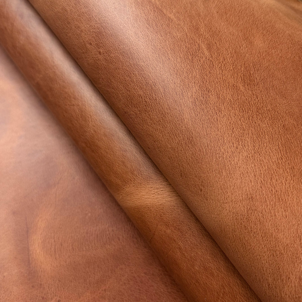 Aragona cognac brown leather featuring a soft, natural grain texture with elegant folds and a smooth matte finish.
