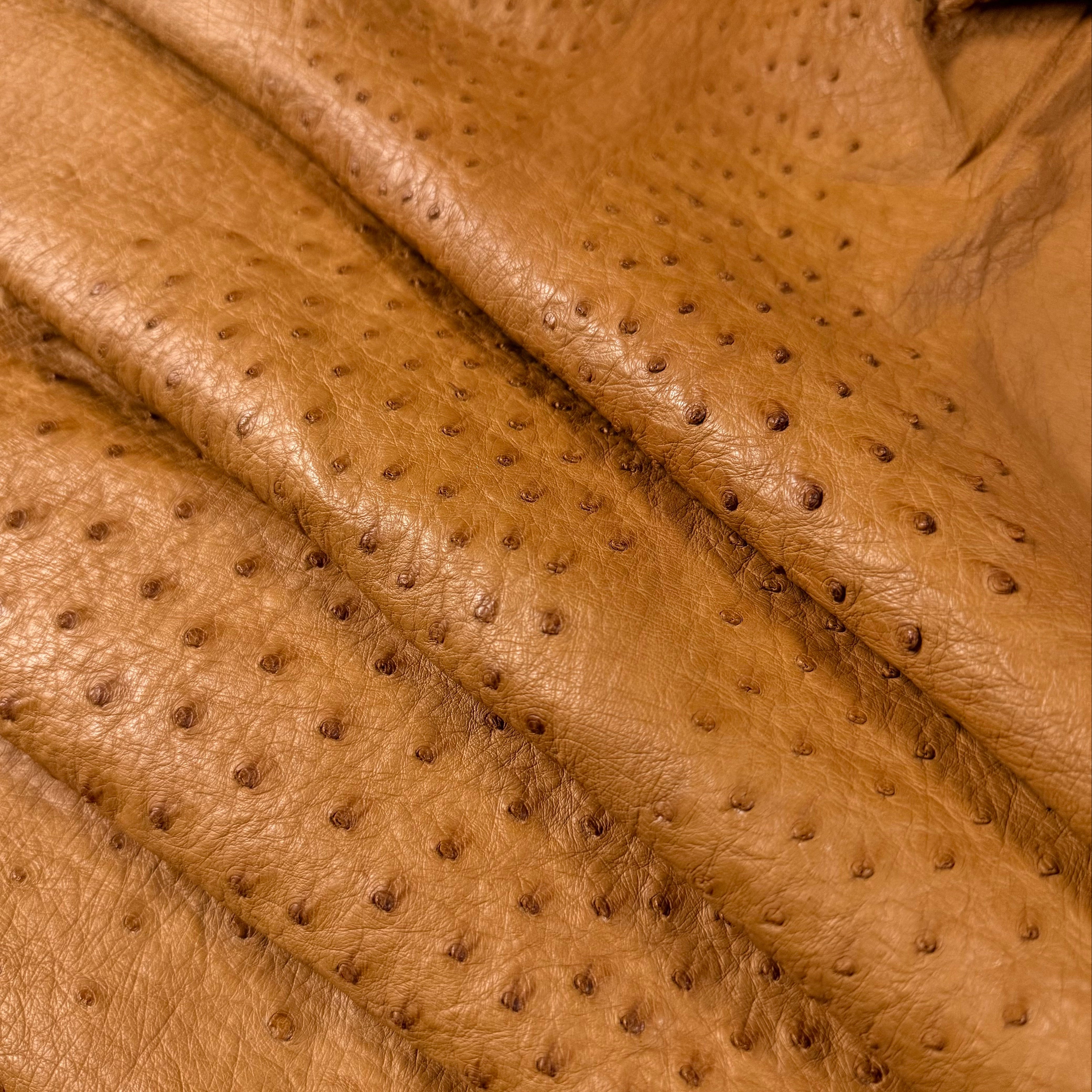 Close-up of genuine full quill ostrich leather in a rich tan color, showing its distinctive textured pattern.