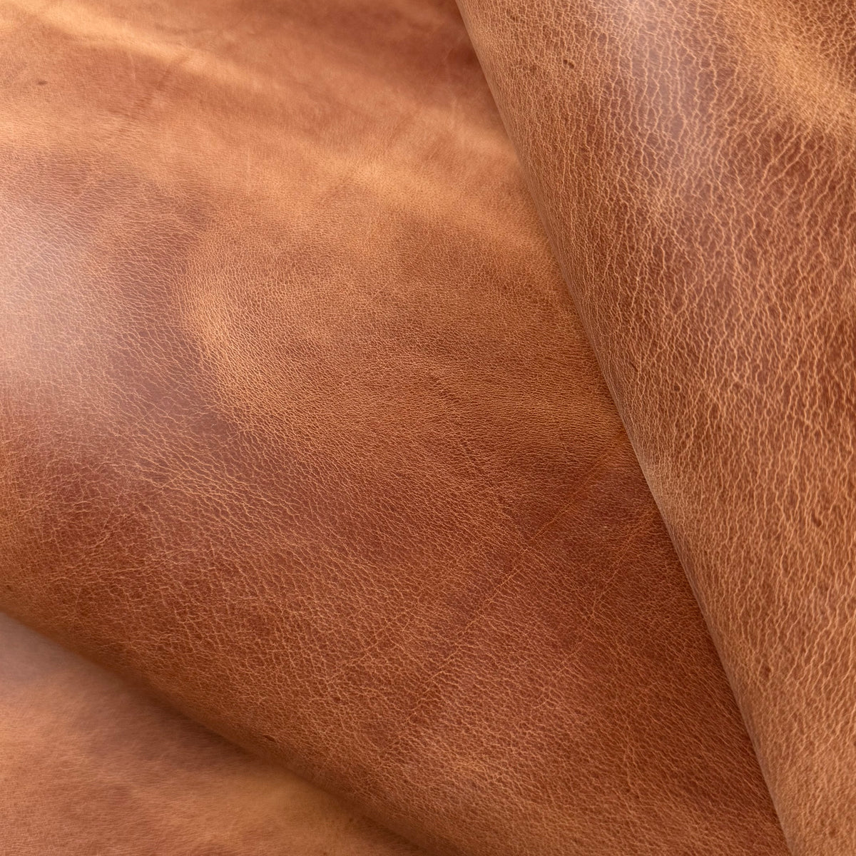 Aragona leather in cognac, featuring a rich, textured surface with natural grain patterns and soft, folded layers.