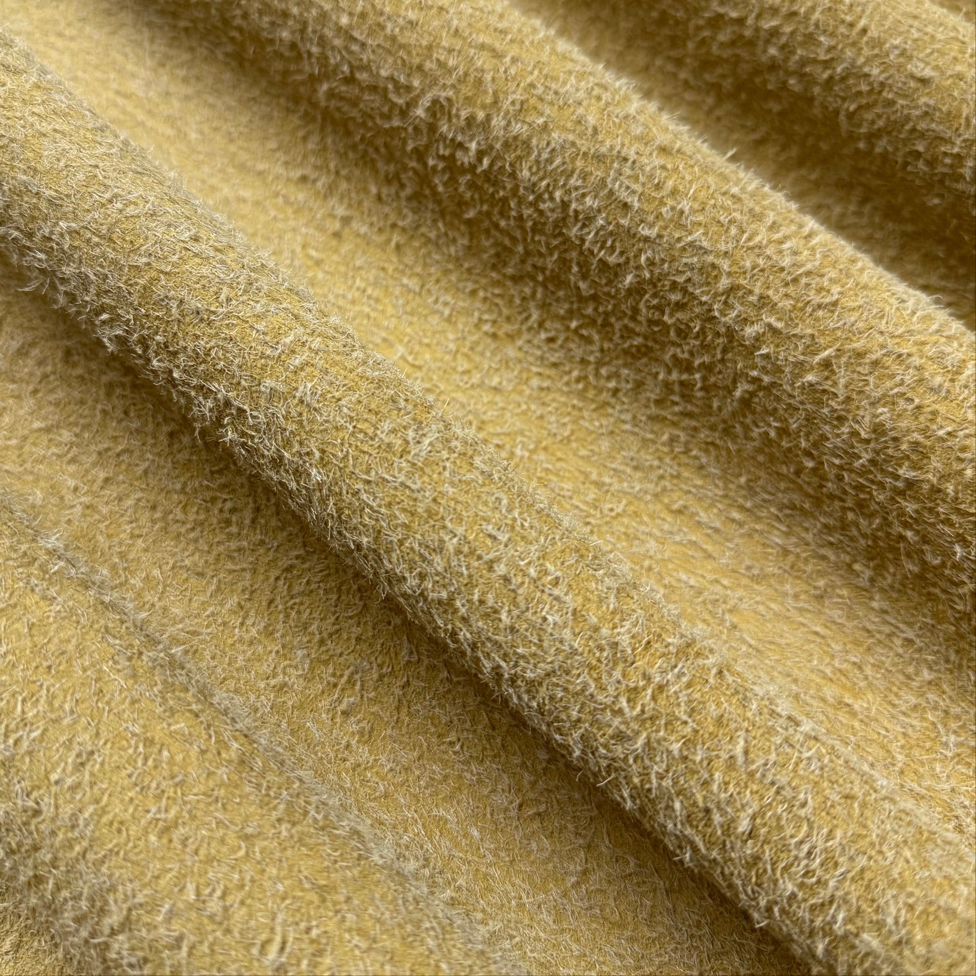 Close-up of a draped Hairy Calf Suede Bend in yellow, showing its shaggy, textured surface.