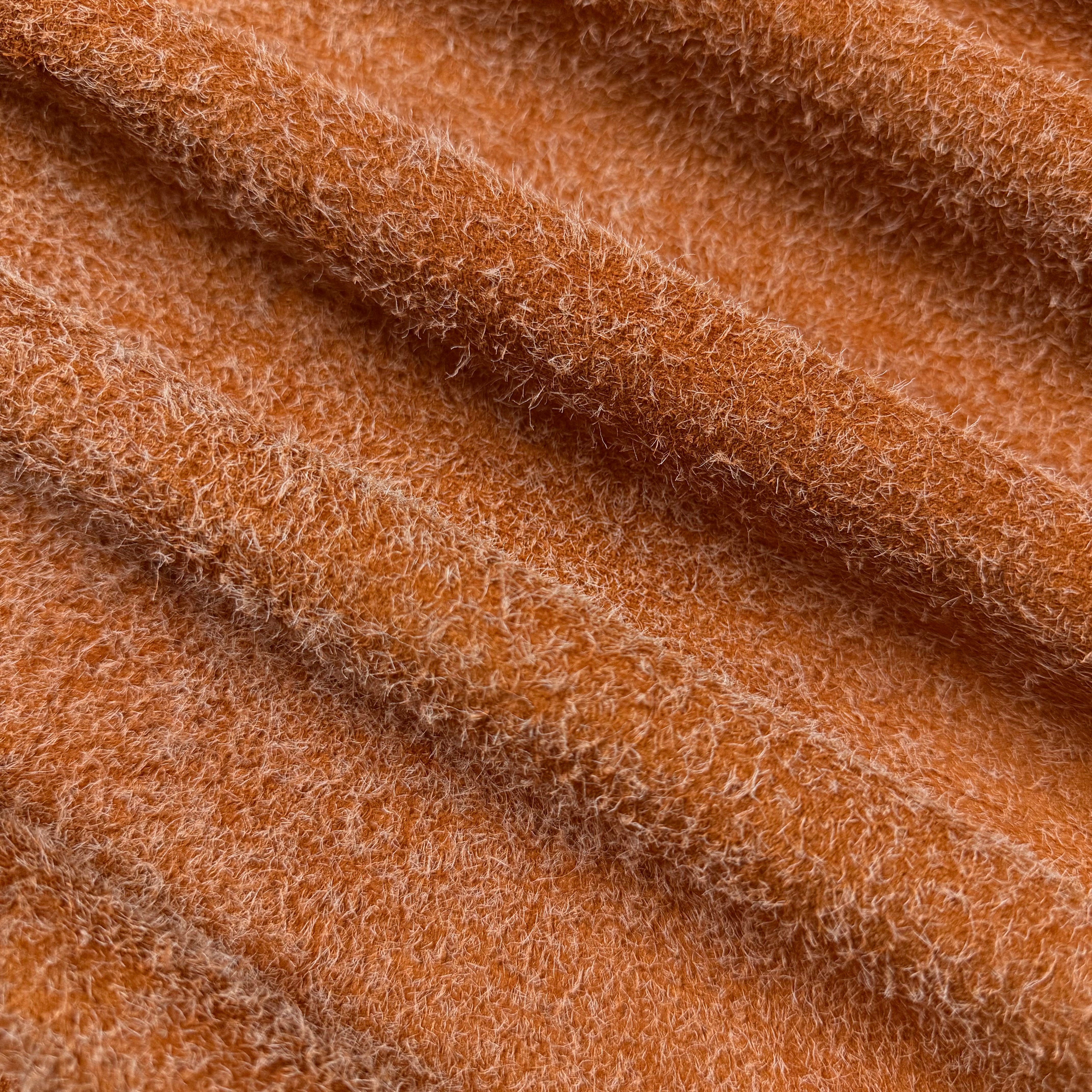 Close-up of a folded Hairy Calf Suede Bend in a warm orange color, showcasing its shaggy, textured surface.