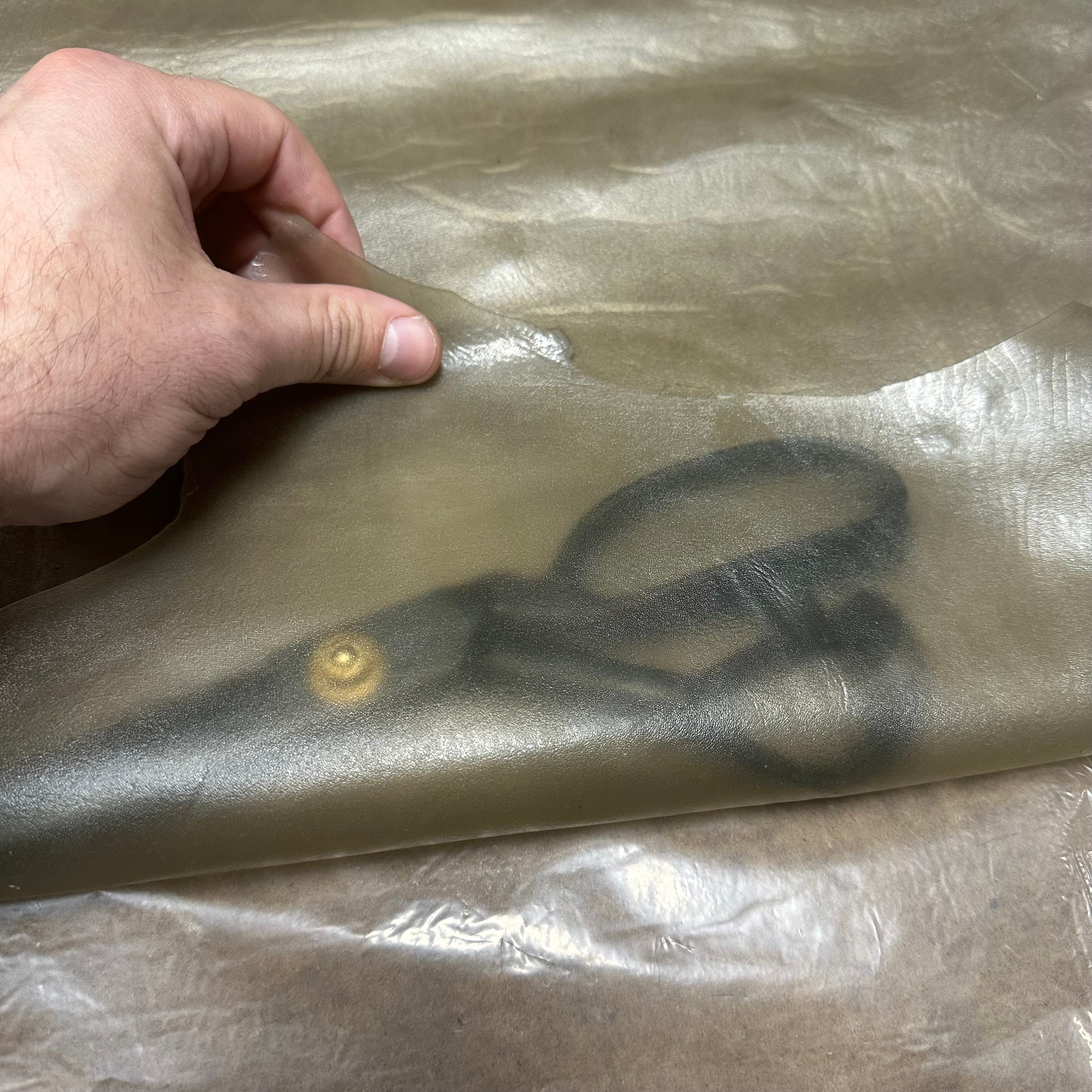 Transparent Lamb Leather in Smoke, 1.5 oz, showing a thin, semi-translucent sheet held by a hand over black scissors.