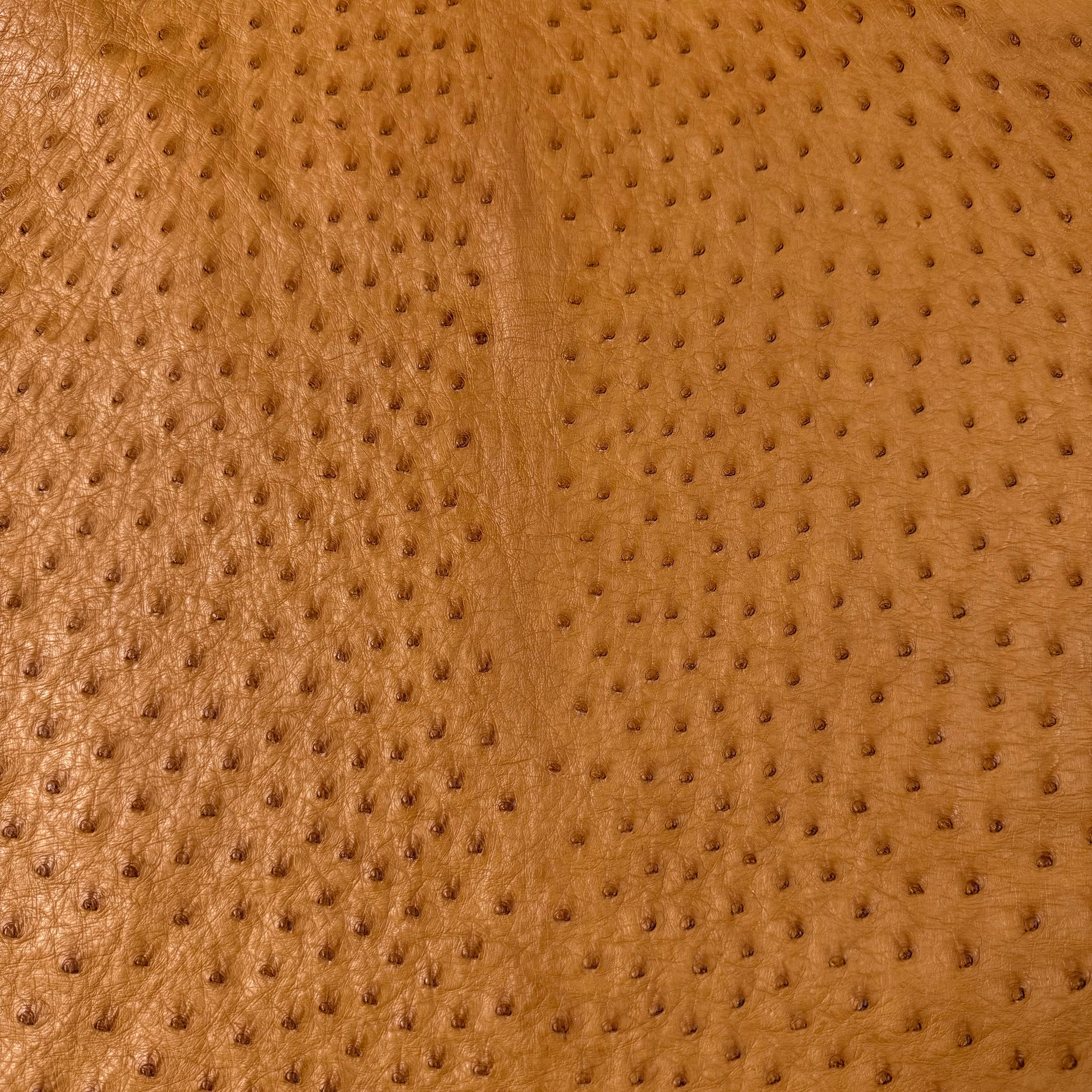 Close-up of genuine full quill ostrich leather in a warm tan color, showcasing its distinctive raised texture.