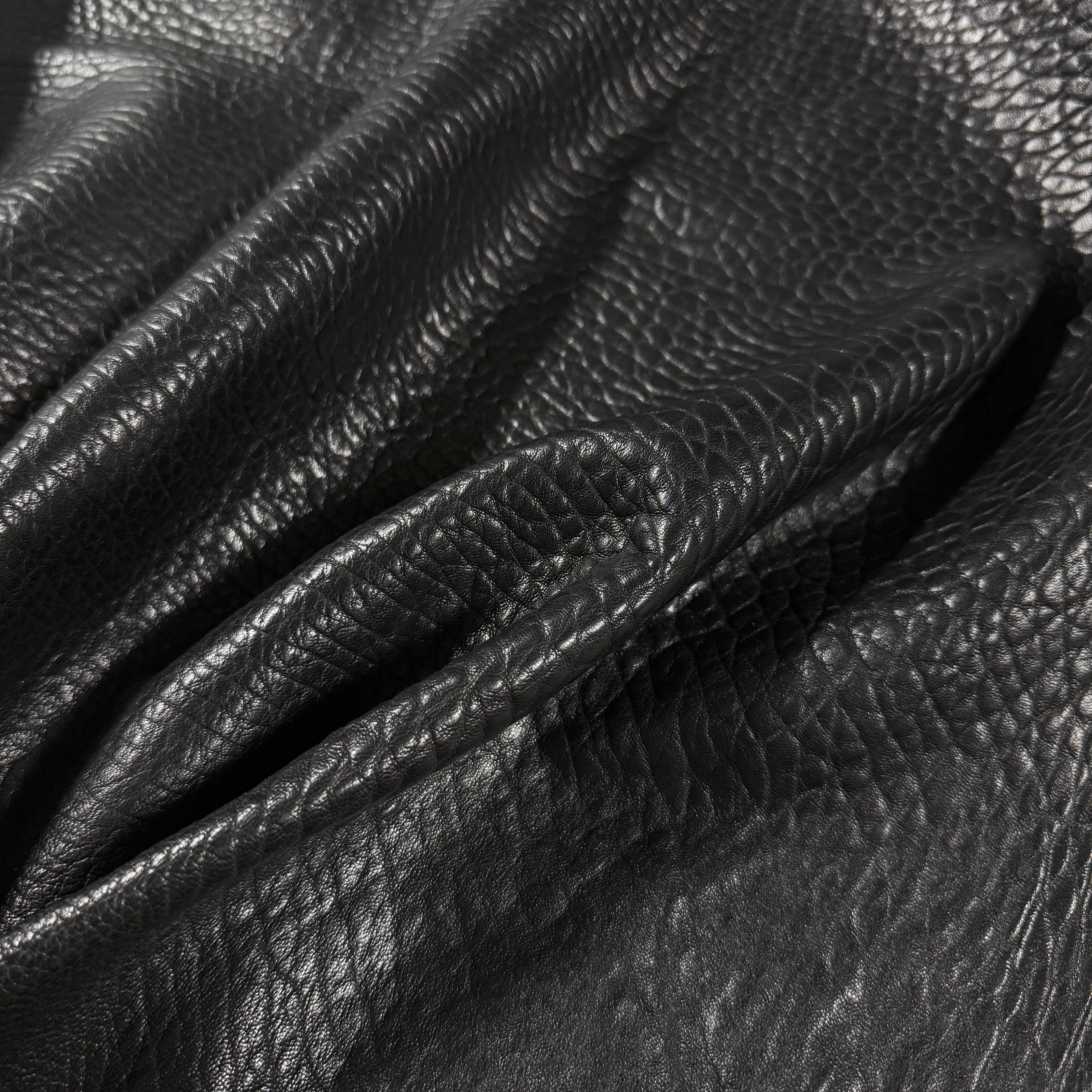 Black shrunken bubble grain veg tan lamb leather with a krispy, textured surface and soft folds.