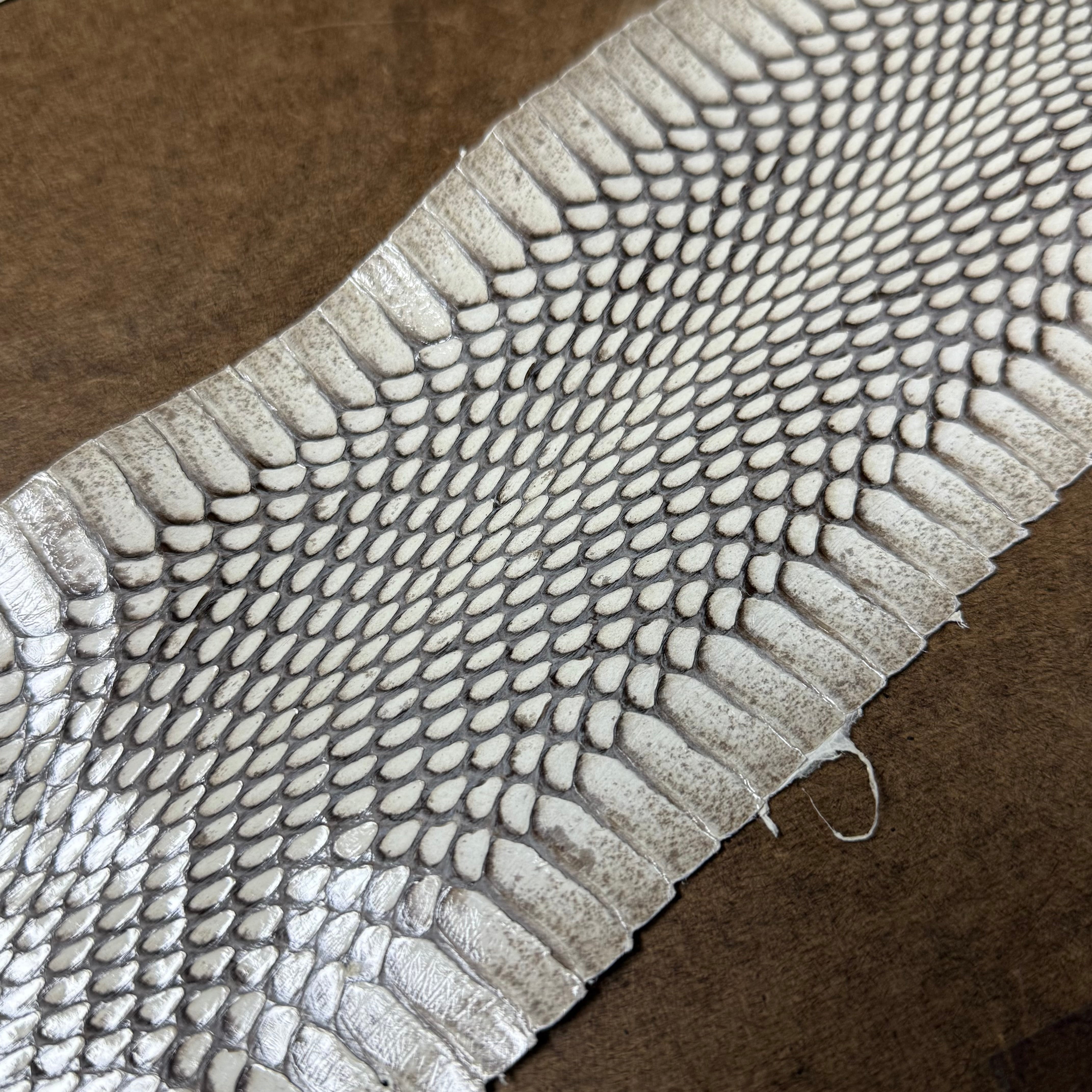 Cobra leather strip in white with detailed natural scale texture, displayed against a brown suede background.