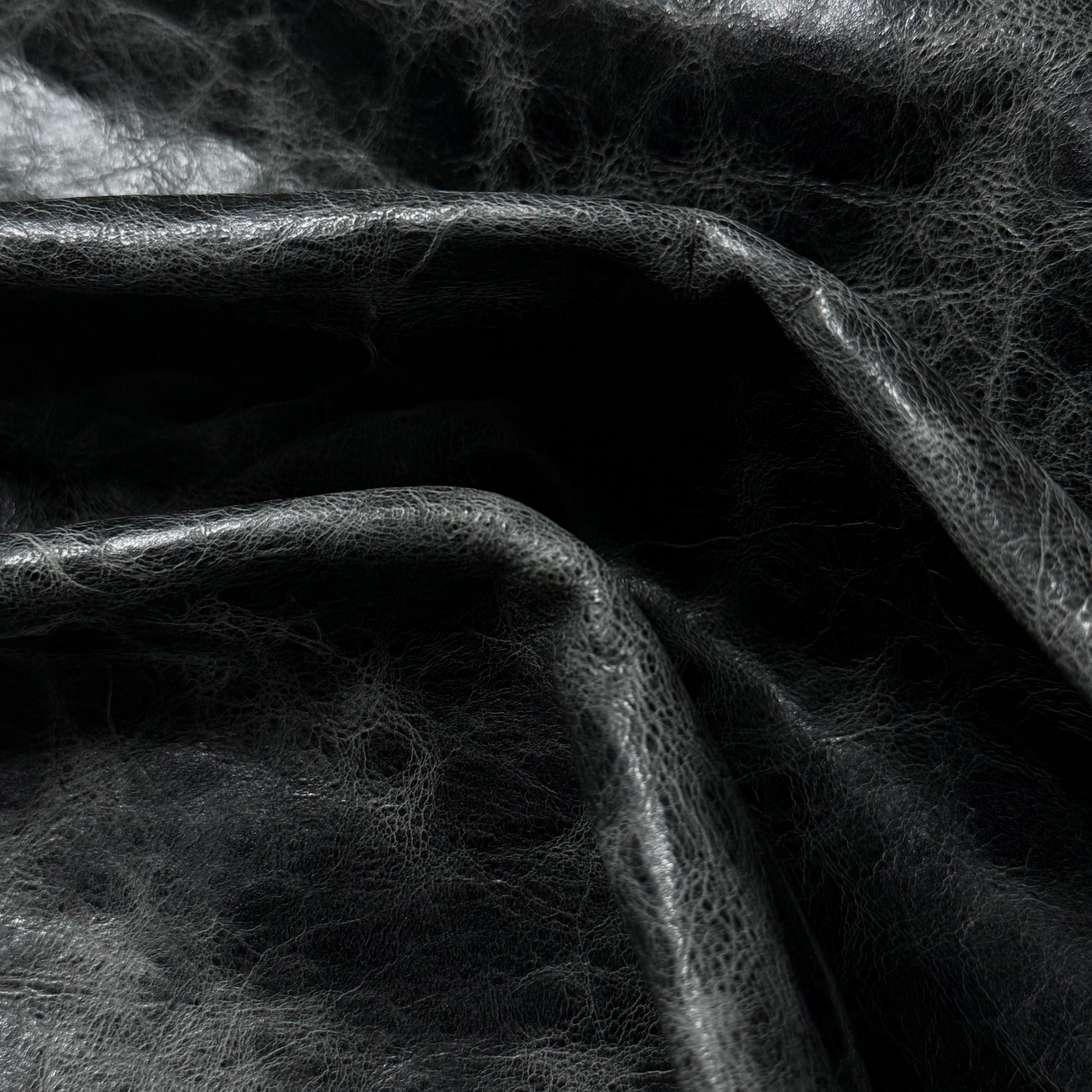 Black Carnauba Waxed Pull-Up Cowhide leather, 2-3 oz, featuring a distressed, textured surface with natural folds.